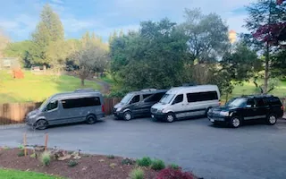 Three Mercedes Sprinter vans and a black Lincoln SUV parked in a row at a winery