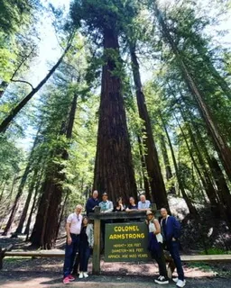 A tour group standing at the Colonel Armstrong tree sign beneath towering redwoods in Sonoma County